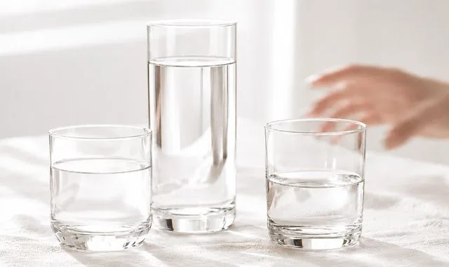 Tri čaše sveže vode različitih veličina na svetlom stolu